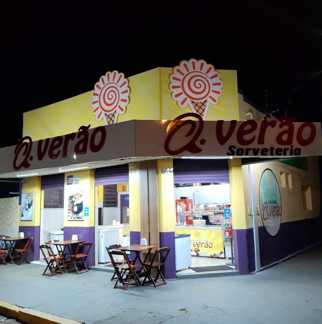 Fachada noturna da Sorveteria Q.verão com letreiro e mesas na calçada